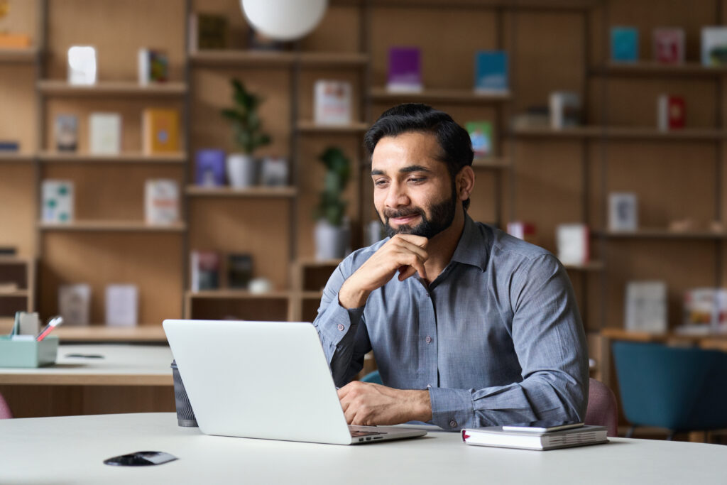 Smiling,Indian,Businessman,Working,On,Laptop,In,Modern,Office,Lobby