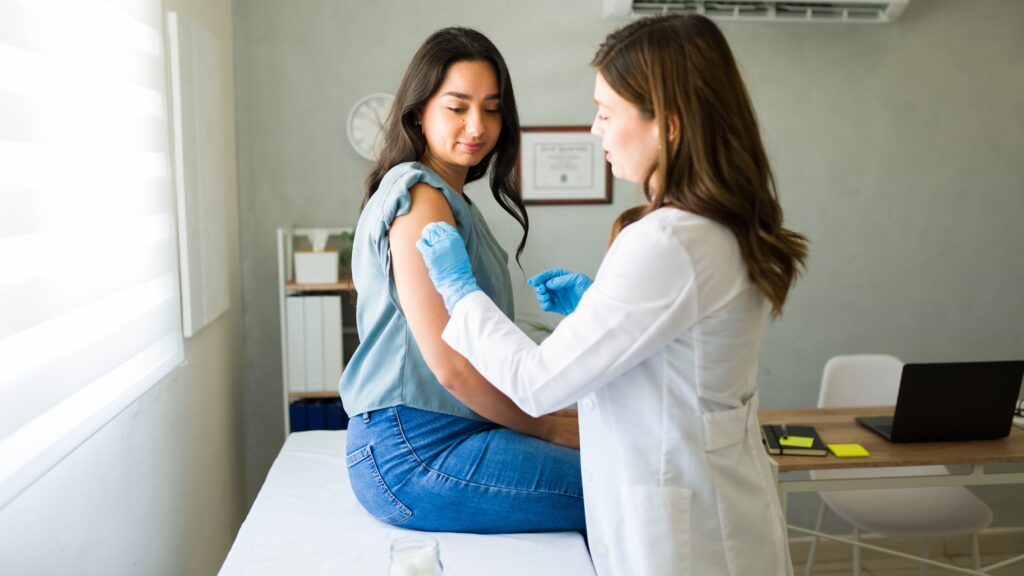 Claiming vaccinations on health insurance. A young woman receives a vaccination in the arm by a female health professional. 