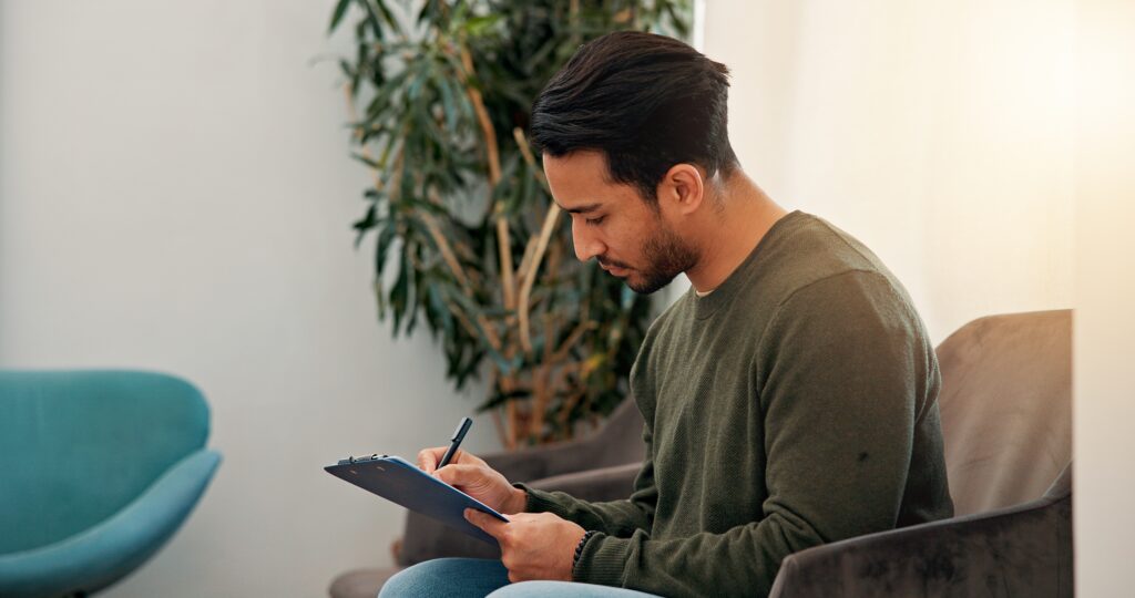 Does health insurance cover vasectomy? A man in a green sweater sits in a waiting room filling out a form. 