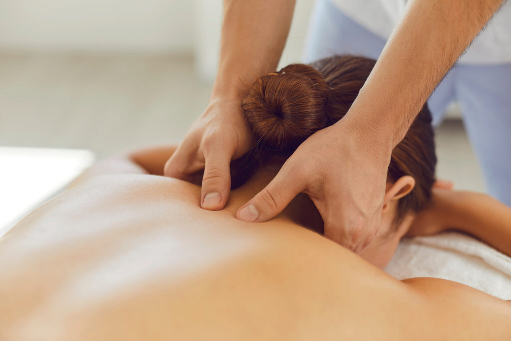What's the best health insurance for remedial massage? A woman lies on massage table, while a man's hands work on muscles in her upper back.