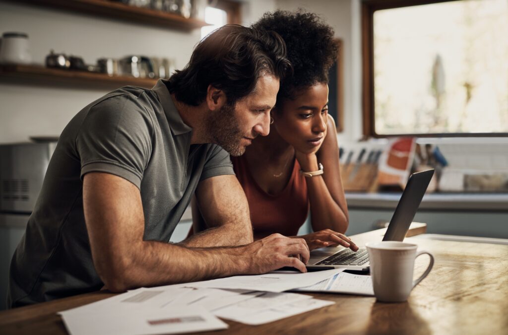 Australian health insurance brands. Are you paying more for a white label brand of health insurance? A couple sit at a table on their laptop, with bills spread around them and a coffee mug.