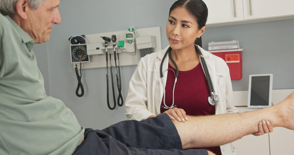 Choosing joint replacement cover. A female physician assesses an older man's knee.