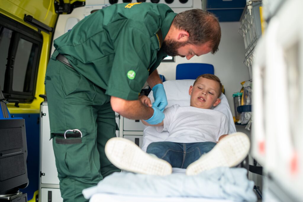 ambulance cost in Australia. A male paramedic supports a young boy on a stretcher in an ambulance.